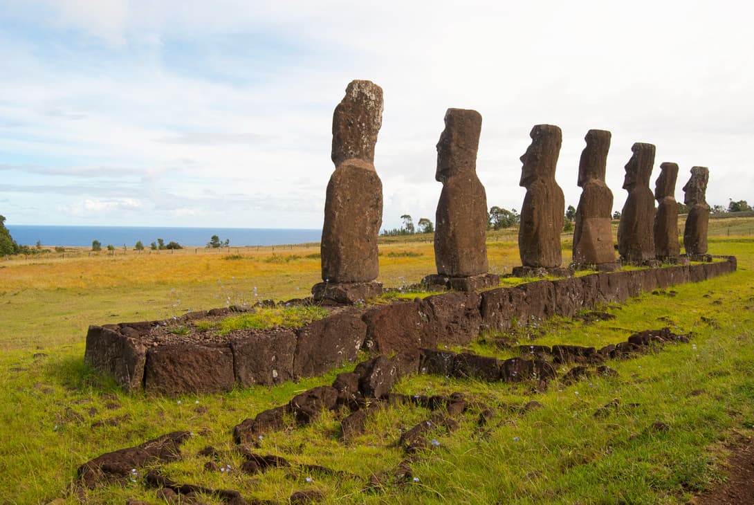 Ahu Akivi moai statues facing ocean with crematorial pits behind monument