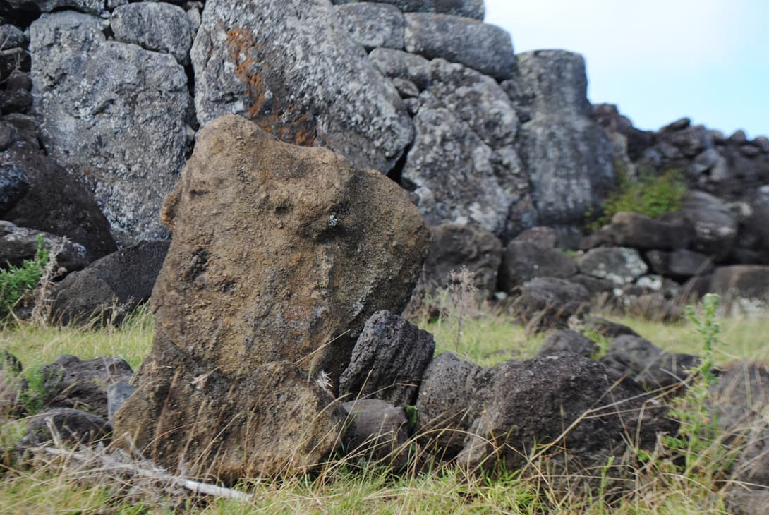 Broken moai statue head with whole statue in rock wall