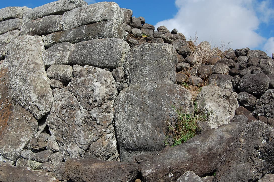 Gray basalt moai statue recycled in ahu rock wall along north coast