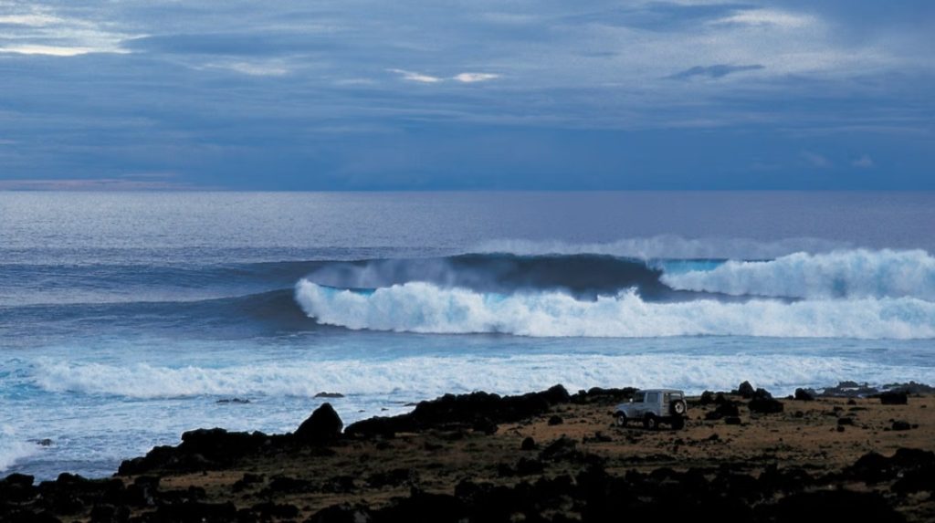 A rocky coastline featuring an off-road vehicle and crashing waves, accompanying tips on surfing equipment for Rapa Nui (Easter Island).