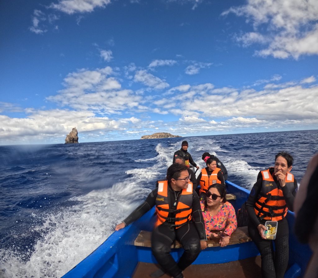 A group of divers in life jackets and wetsuits riding a boat toward Motu Nui in Rapa Nui.