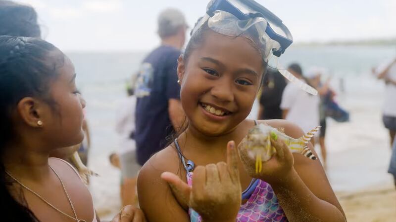 Happy 9-year-old girl on the beach with a snorkel mask holding a fish and gesturing the shaka sign rapa nui style.