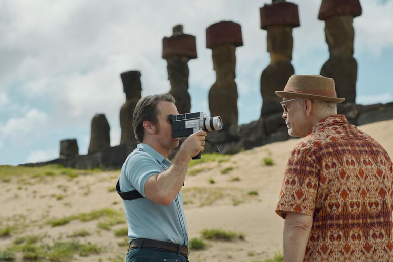Sam Rockwell using a movie camera to film John Malkovich in front of Ahu Nau Nau at Anakena Beach in Wild Horse Nine