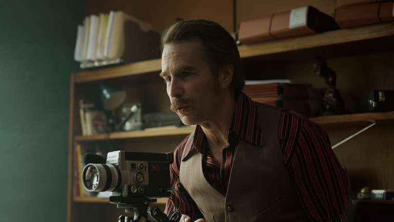 Sam Rockwell operating an vintage movie camera inside a 1970s office setting in Wild Horse Nine