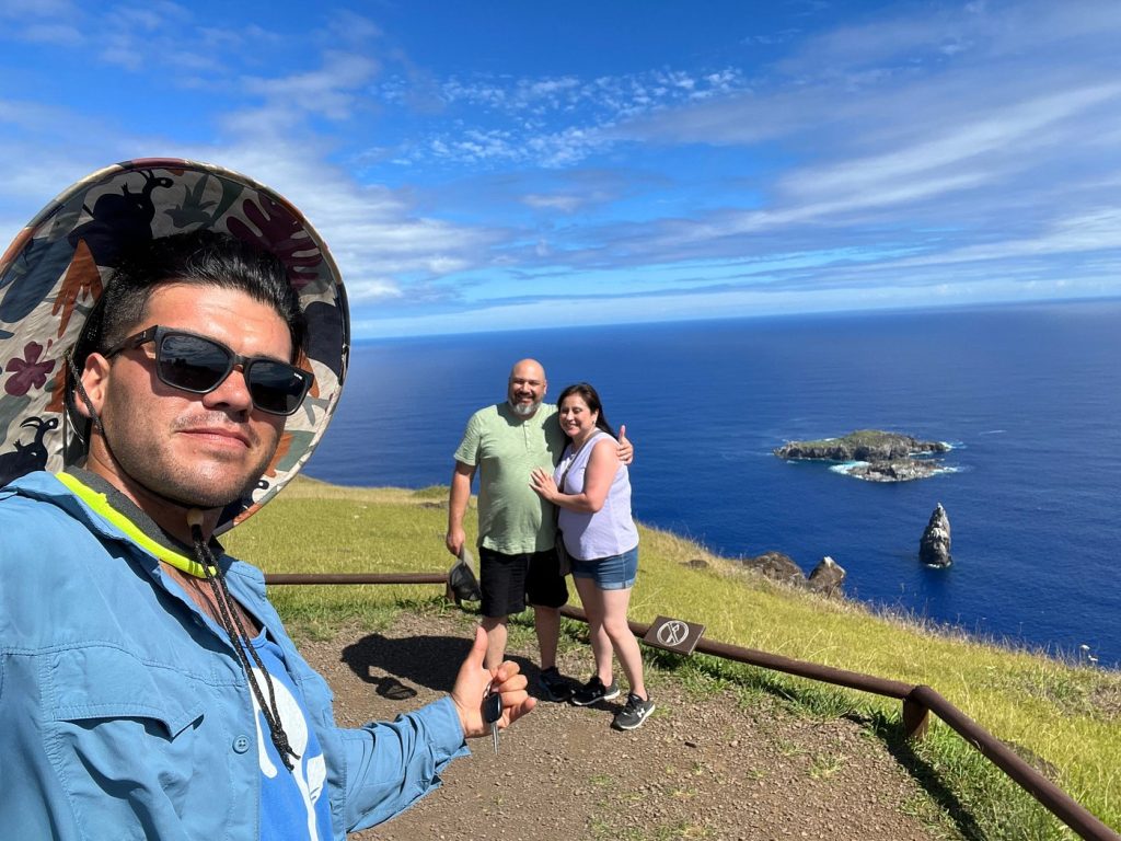 A tour guide taking a selfie with tourists at the Rano Kau viewpoint, overlooking the Pacific Ocean and Motu Nui islets.