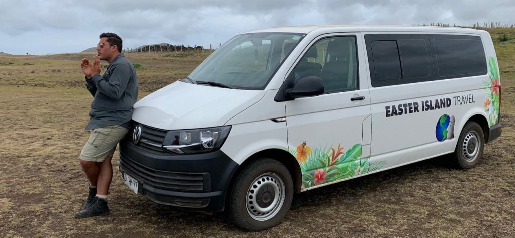 A tour guide leaning against a white Easter Island Travel van parked on an open field during a private excursion.