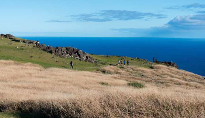 Tourists walking along a scenic marked trail on the grassy hills of Rapa Nui National Park overlooking the Pacific Ocean.