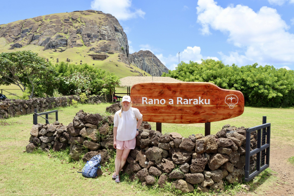 Tourist standing beside a stone wall near the Rano Raraku sign during an archaeological route in Rapa Nui.