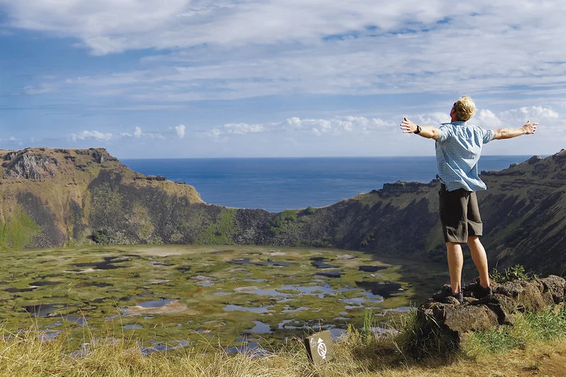 Tourist standing on a rock at Rano Kau with arms open, looking toward the vast Pacific Ocean and enjoying the wind in Rapa Nui.
