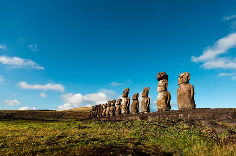 The fifteen moai of Ahu Tongariki viewed from below against a clear blue sky during an archaeological route in Rapa Nui.