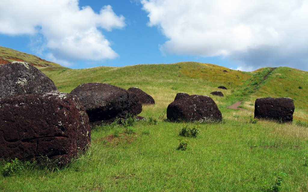 Red scoria pukao scattered across the green slopes of Puna Pau, the quarry where the moai headdresses were carved in Rapa Nui.