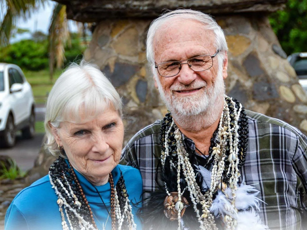 Nancy Weber y su esposo Roberto sonriendo a la cámara mientras lucen múltiples collares de conchitas de mar tradicionales de Rapa Nui sobre sus cuellos.